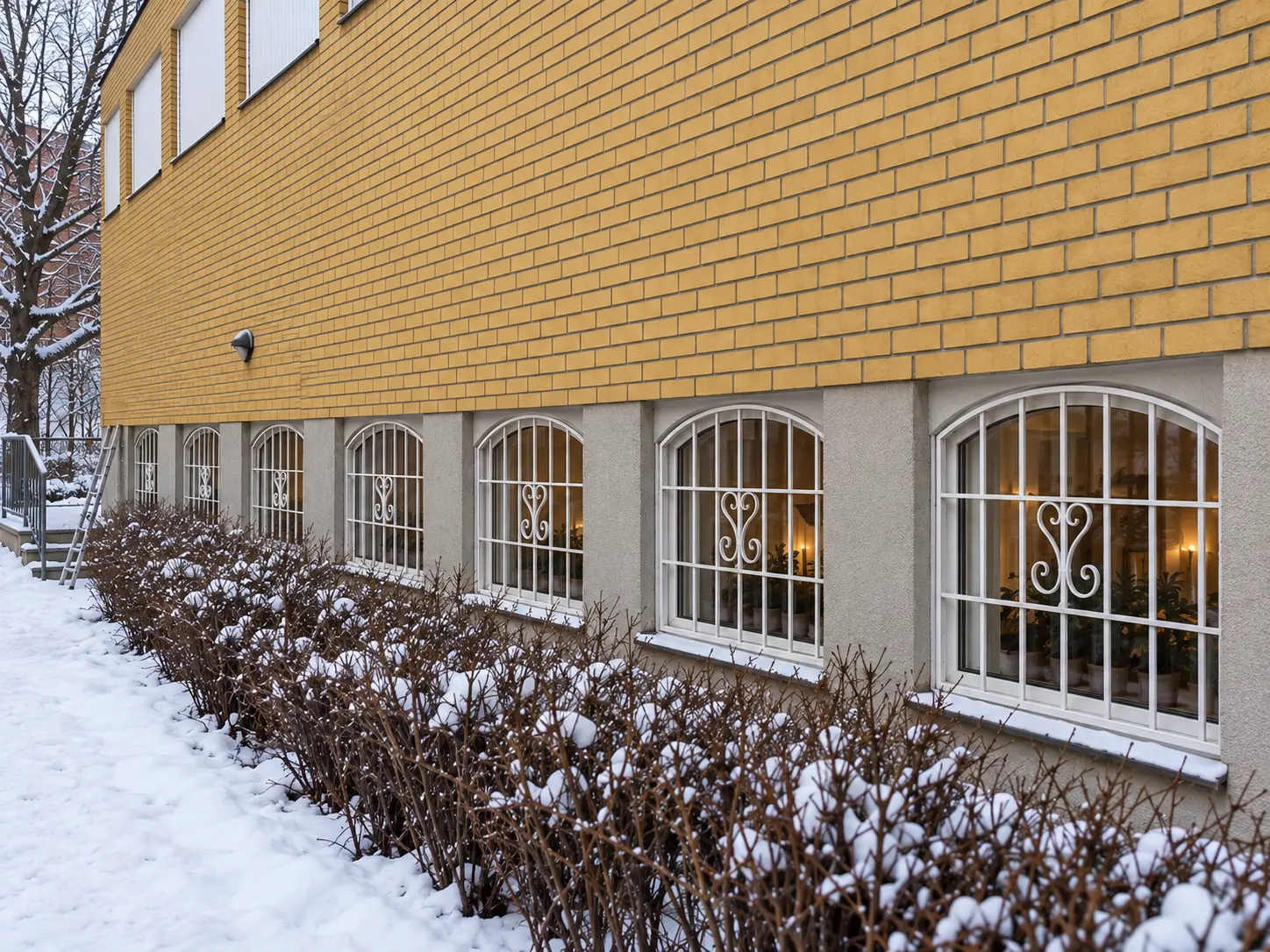 Vita fönstergaller på bågformade källarfönster längs gulmurad fastighet i Stockholm